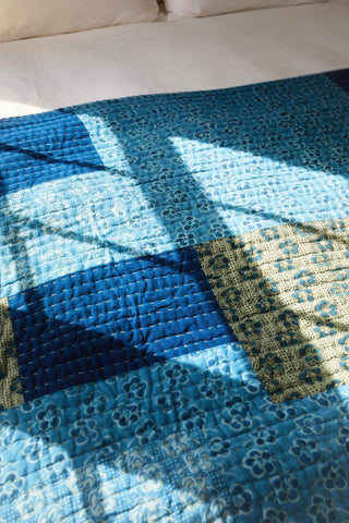Close-up of a blue and yellow quilt with geometric patterns on a bed.