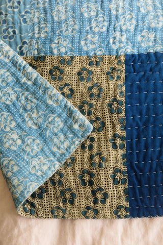Close-up of a quilt with blue and beige patterns on a beige surface.