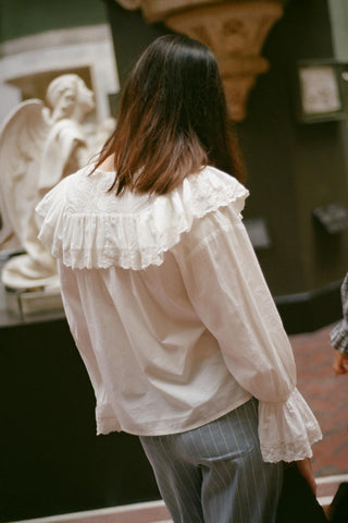 Person wearing a white blouse with ruffled details in an indoor setting