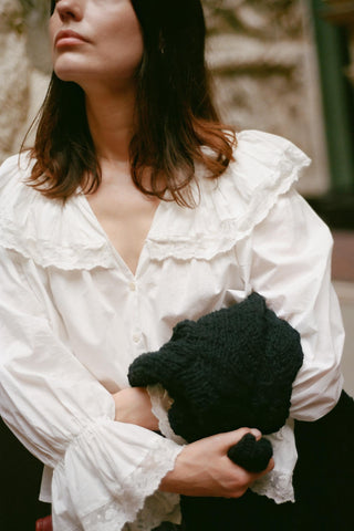 Woman wearing a white blouse holding a black knitted item.