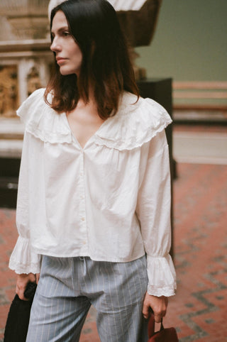 Woman wearing a white blouse with ruffled details and gray plaid pants.