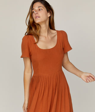 Woman wearing a rust-colored dress against a plain background