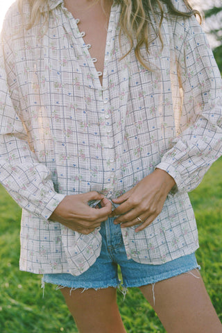 Person wearing a plaid shirt and denim shorts standing in a grassy area
