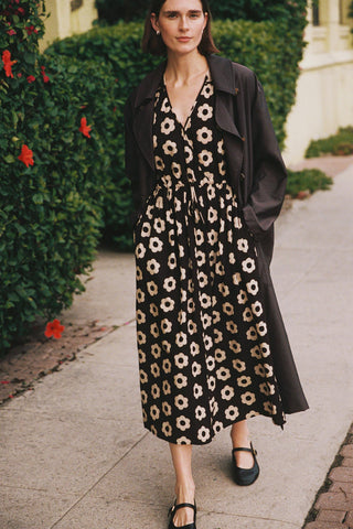 Woman wearing a floral dress with a black coat on a sidewalk.