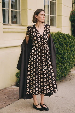 Woman wearing a black floral dress with a long black coat outdoors.