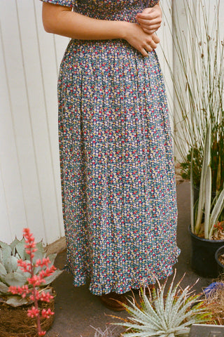 Person wearing a floral dress standing outdoors with plants in the background