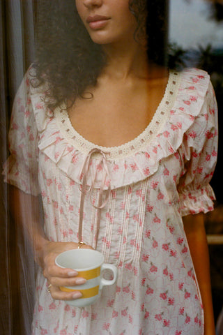 Woman wearing a low scoop floral dress holding a mug with a blurred background