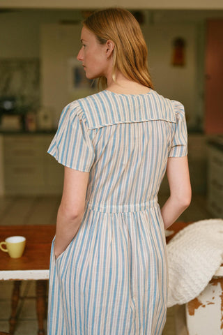 Woman wearing a blue and white striped dress in a room with a table and chair.