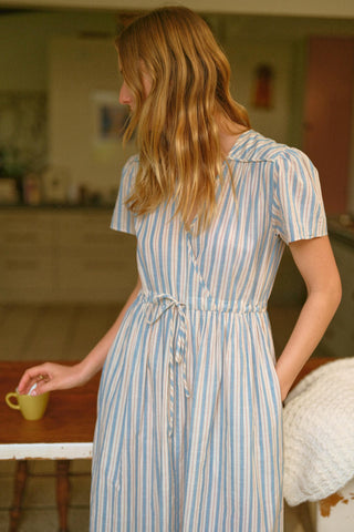 Woman in a striped dress holding a cup in a kitchen setting