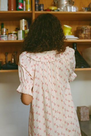 Back shot of a Person wearing a floral dress standing in front of a shelf with various items.