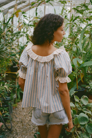 Woman wearing a striped blouse with lace details in a greenhouse setting