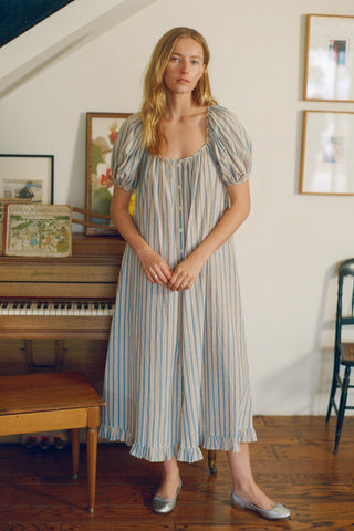 Woman in a striped dress standing in a room with a piano and framed pictures on the wall.