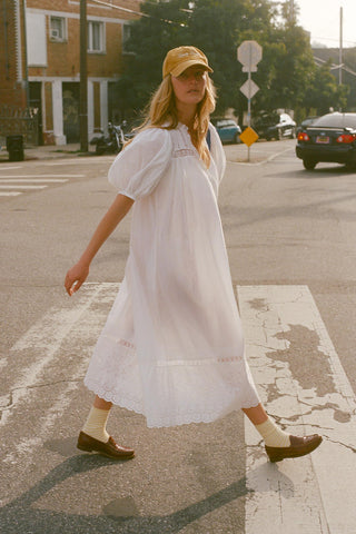 Woman in a white dress and yellow cap walking on a street.