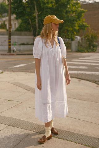 Woman in a white dress and yellow cap walking on a sidewalk.