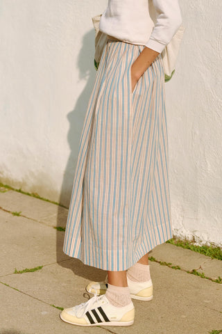 Person wearing a striped skirt and Adidas sneakers against a white wall.