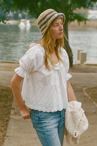 Woman wearing a white blouse, blue jeans, and a striped hat by a lake.