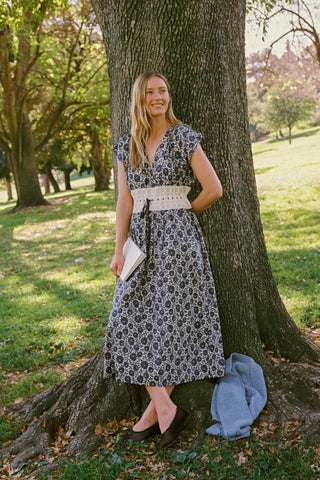 Woman in a floral dress standing next to a tree in a park