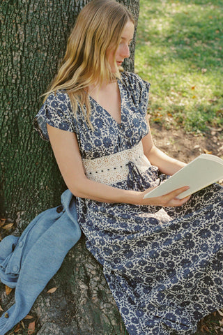 Woman in a floral dress reading a book against a tree