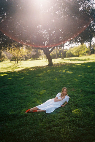 Woman in a white dress lying on grass under a tree 
