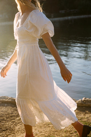 Woman in a white dress walking by a body of water