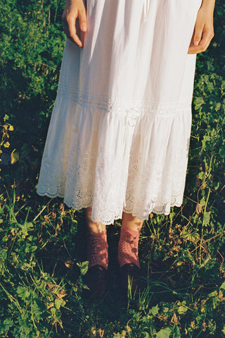 Person wearing a white dress and brown boots standing in a grassy field