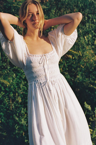 Woman in a white dress standing against a green natural background