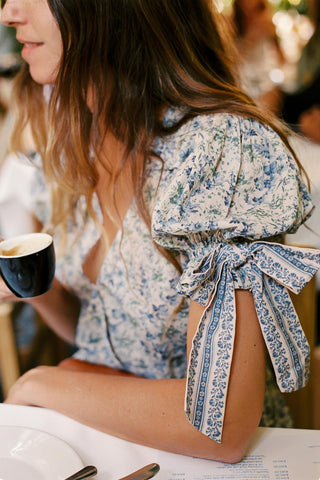 Woman wearing a floral headscarf sitting at a table with a blurred background