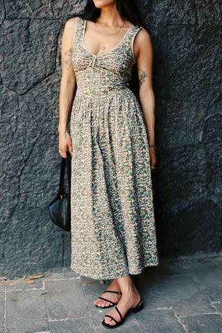 Woman wearing a green patterned dress against a dark stone wall.