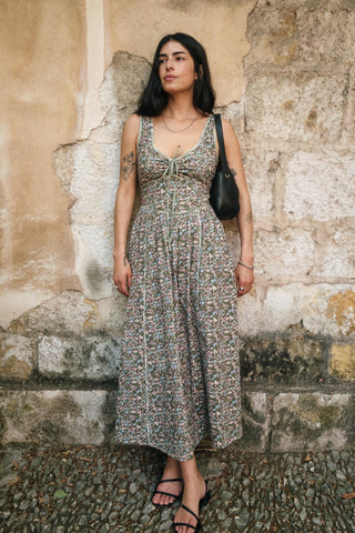 Woman in a green patterned dress standing against a stone wall.