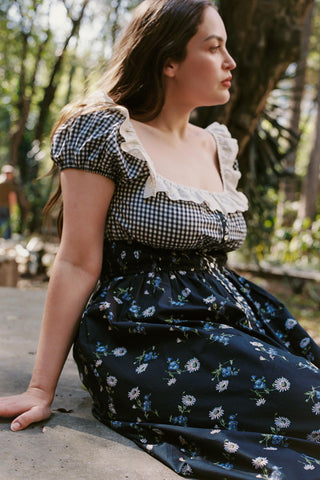 Woman sitting outdoors wearing a checkered top and floral skirt.
