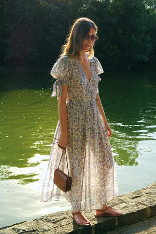 Woman in a floral dress standing by a body of water with trees in the background