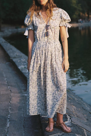 Woman wearing a floral dress standing by a body of water.