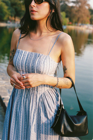 Woman in a blue and white striped dress standing by a body of water.
