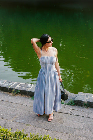 Woman in a blue dress standing by a body of water.