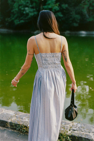 Woman in a long dress standing by a body of water with trees in the background