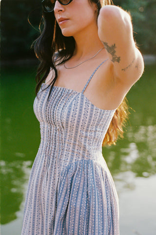 Woman in a blue patterned dress standing by a body of water.