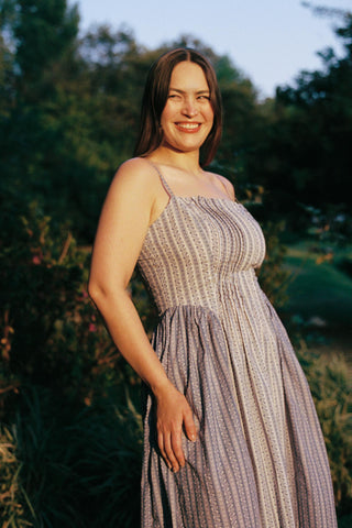 Woman in a patterned dress standing outdoors with greenery in the background