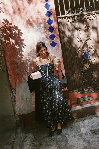 Woman in a long black dress with white patterns standing in front of a decorative metal gate.