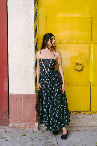 Woman in a floral dress standing in front of a yellow door.
