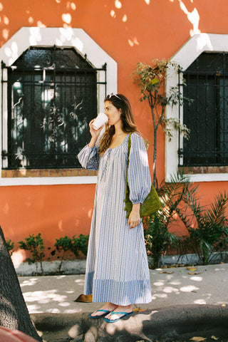 Woman in a blue and white striped dress standing in front of an orange building.
