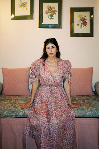 Woman in a floral dress sitting on a couch with decorative pillows and framed artwork in the background.