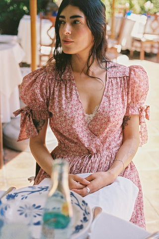 Woman in a floral dress sitting at an outdoor table with a scenic background