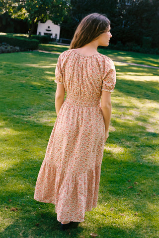 Woman in a floral dress standing on grass with a bench in the background