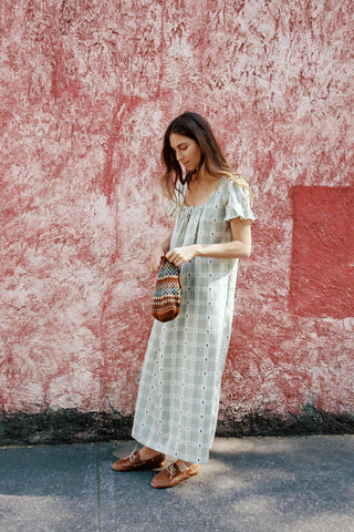 Woman in a long green dress standing against a textured pink wall.
