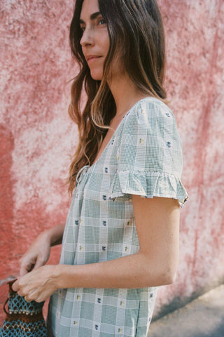 Woman wearing a light green checkered dress against a pink wall.