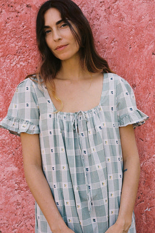 Woman wearing a green patterned dress against a pink textured wall