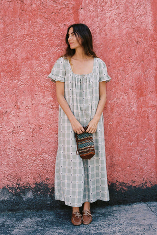 Woman in a long, green colored dress standing against a textured pink wall.