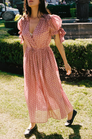 Woman wearing a pink floral dress standing on grass with bushes in the background