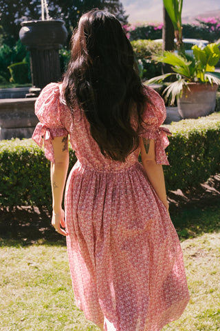Woman in a pink floral dress standing in a garden