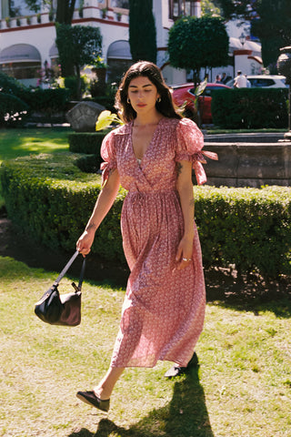 Woman in a pink dress walking outdoors with greenery and buildings in the background